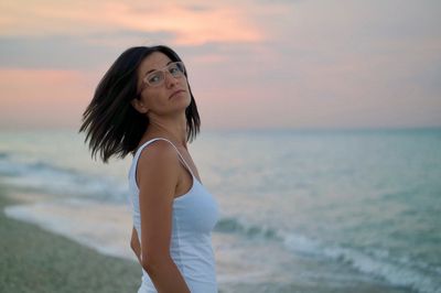 Young woman standing on beach against sky during sunset