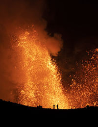 Silhouettes of anonymous travelers standing against orange fume of active volcano in iceland
