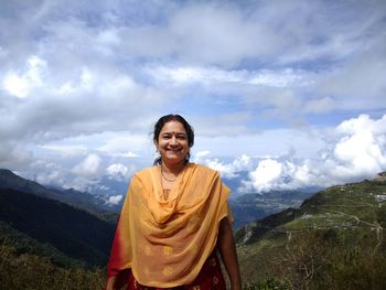 Portrait of smiling woman standing on mountain against cloudy sky