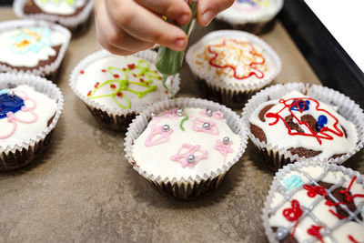 A child squeezes colored frosting from a tube onto chocolate brown cupcakes covered white frosting.