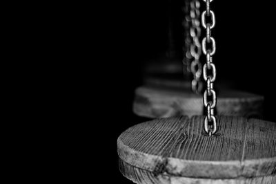 Close-up of wood hanging to chains against black background