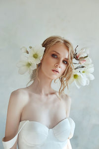 Close-up portrait of bride with flowers on head against wall