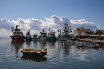 Fishing boats moored at harbor against sky