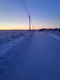 Snow covered road against sky during sunset