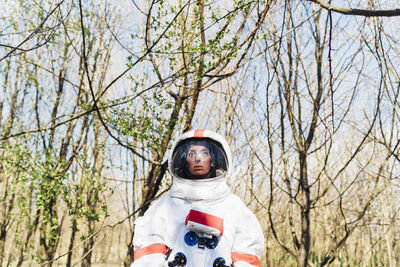 Female astronaut wearing space suit and helmet standing in forest