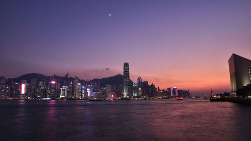 Illuminated buildings by river against sky at night