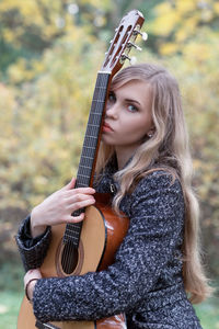 Portrait of beautiful young woman holding guitar outdoors