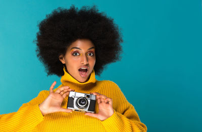 Portrait of shocked woman holding camera against blue background