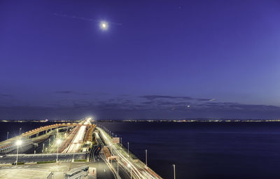 Illuminated bridge by sea against sky at night