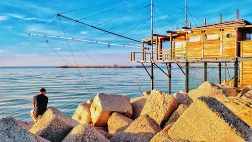 Rear view of man standing on rock by sea against sky