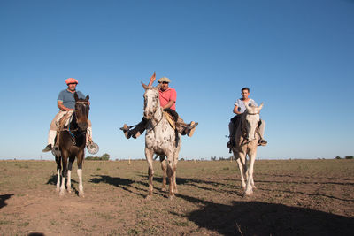 Men riding horses on field against clear sky