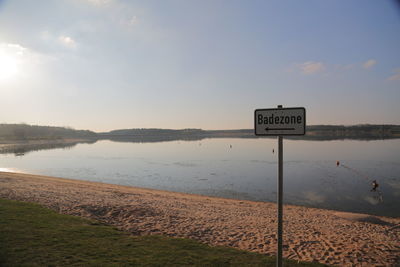 Information sign by sea against sky