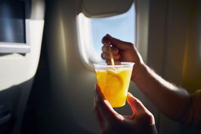 Dring during flight. man holding coctail against airplane window.