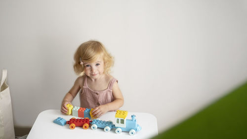 Pretty caucasian 1,2 year old with blond curly hair playing with colourful construction cubes, toys 