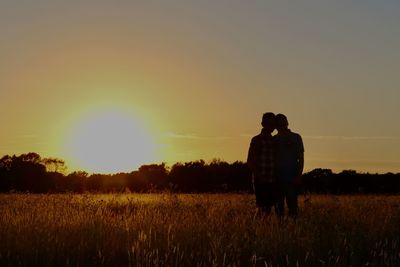 Rear view of man standing on field against sky during sunset