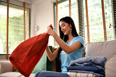 Woman folding dress while sitting on sofa at home