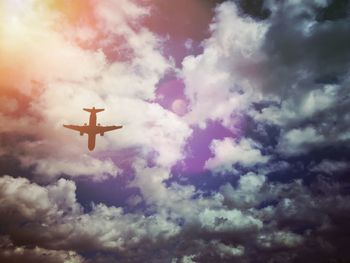 Low angle view of bird flying against cloudy sky