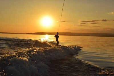 Silhouette teenage boy surfing at sea against sky during sunset