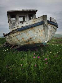 Abandoned boat moored on field against sky
