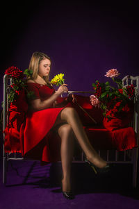 Woman looking at flower while sitting on sofa against wall