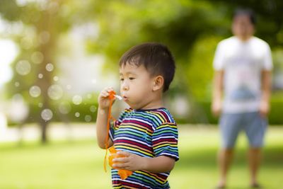 Cute boy holding bubbles while standing outdoors
