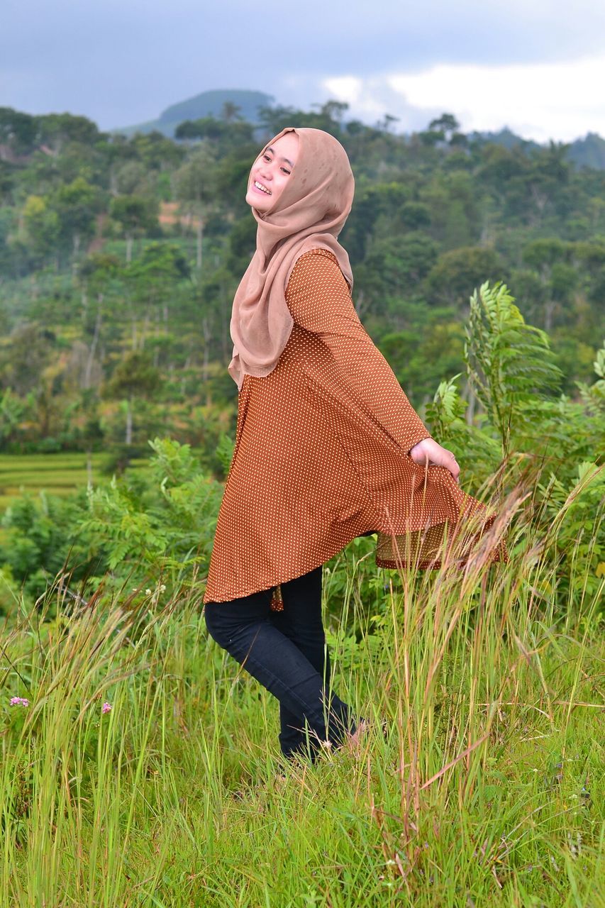 grass, lifestyles, leisure activity, casual clothing, field, young adult, full length, standing, mountain, young women, focus on foreground, dress, landscape, sky, arms outstretched, side view, grassy, person