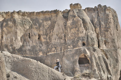 Low angle view of woman photographing on cliff against sky