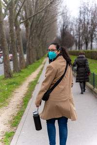 Woman walks down path in a winter coat and covid mask