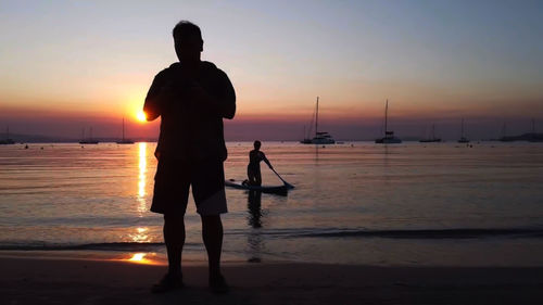 Silhouette people standing on beach against sky during sunset