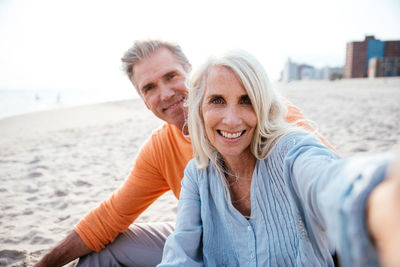 Portrait of smiling couple sitting at sandy beach