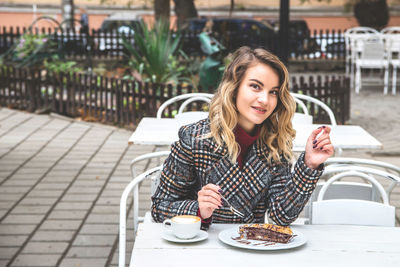 Portrait of young woman having dessert with coffee at outdoor cafe