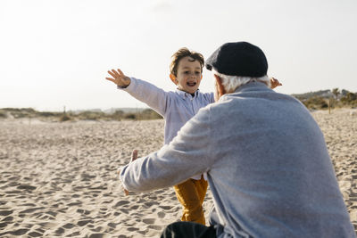 Portrait of little boy running into his grandfather's arms on the beach