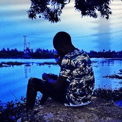 Side view of man looking at lake against sky