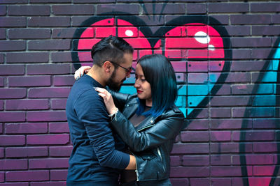 Young couple kissing against brick wall