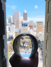 Reflection of person photographing modern buildings against sky