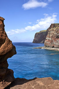 Rock formations by sea against blue sky