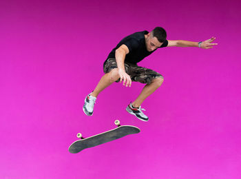 High angle view of young man jumping over pink background