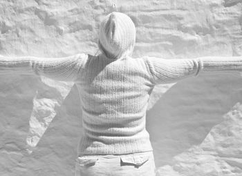 Rear view of woman with arms outstretched standing by white wall