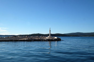 Lighthouse by sea against clear sky