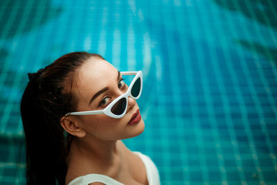 High angle portrait of young woman wearing sunglasses in swimming pool