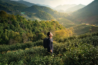 Young man standing by plants against landscape and sky