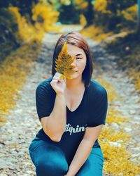 Portrait of young woman holding autumn leaf on footpath