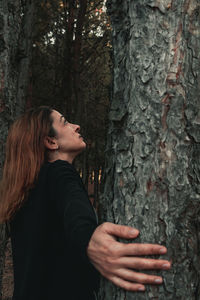 Side view of woman standing by tree trunk in forest