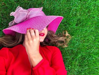 Close-up of woman wearing pink hat while lying on grassy field