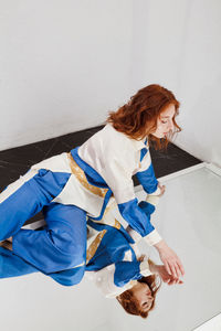 Full length of young woman sitting on mirror against wall