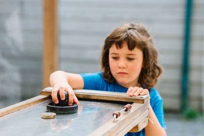 Attentive little girl with brown hair in blue t shirt playing air hockey in entertainment center in daylight