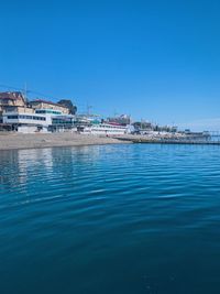 Sea by buildings against clear blue sky