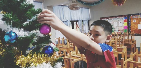 Close-up of boy decorating christmas tree in classroom at school