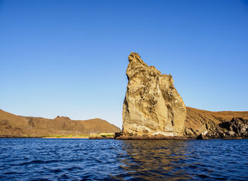 Rock formation in sea against clear blue sky