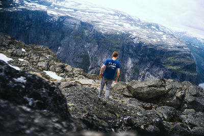 Rear view of man standing on rock against mountains